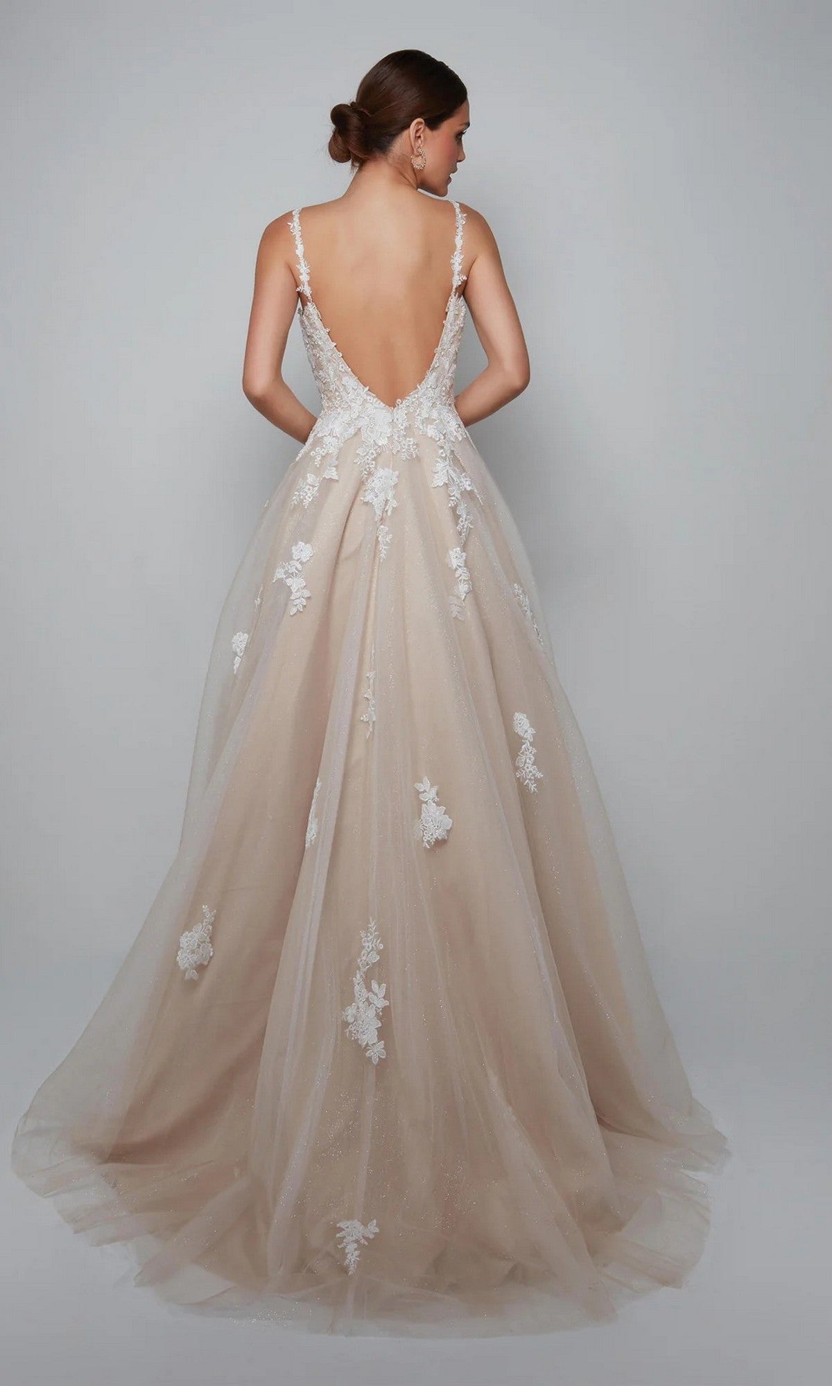 A woman wears the Long White Dress: Alyce 7084, a backless, floor-length bridal ball gown with floral lace appliqués and a sweetheart neckline, standing against a plain gray background.